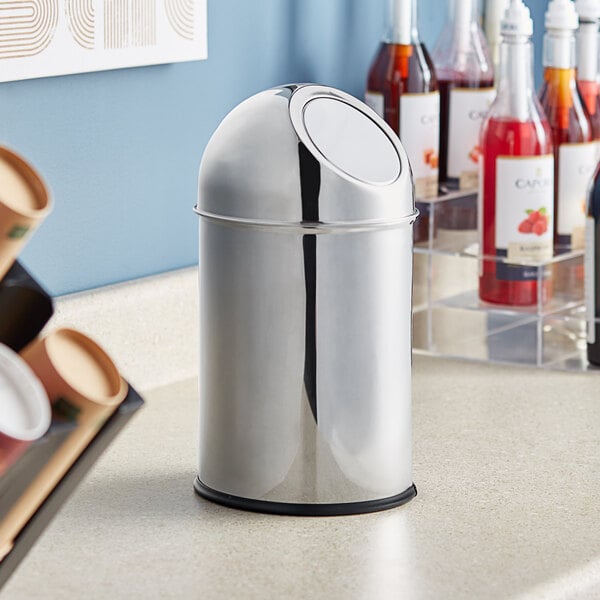 A silver Clipper Mill stainless steel trash can on a counter with drinks.