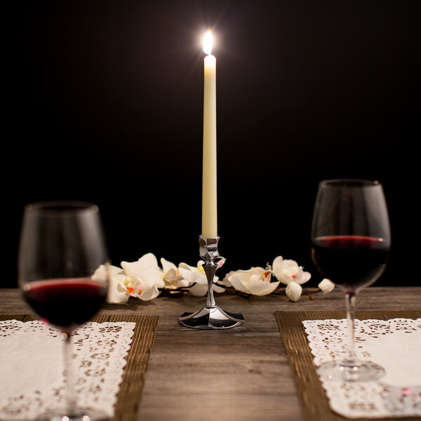 A lit ivory Hyoola taper candle on a table set with wine glasses and flowers.