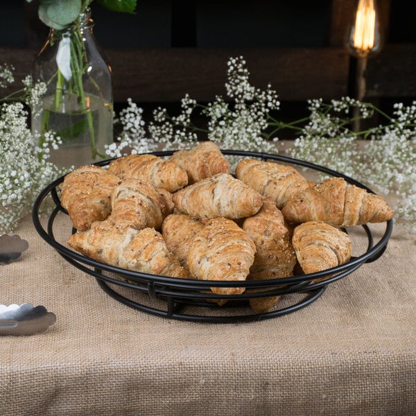 A black Clipper Mill round wire basket filled with croissants.