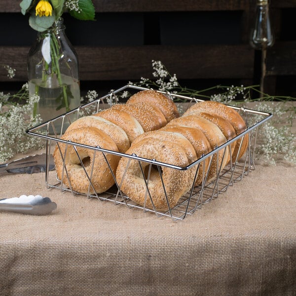 A Clipper Mill chrome plated iron square wire basket filled with bagels on a table.