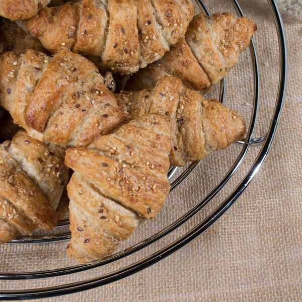 A Clipper Mill chrome plated iron round wire basket filled with croissants.