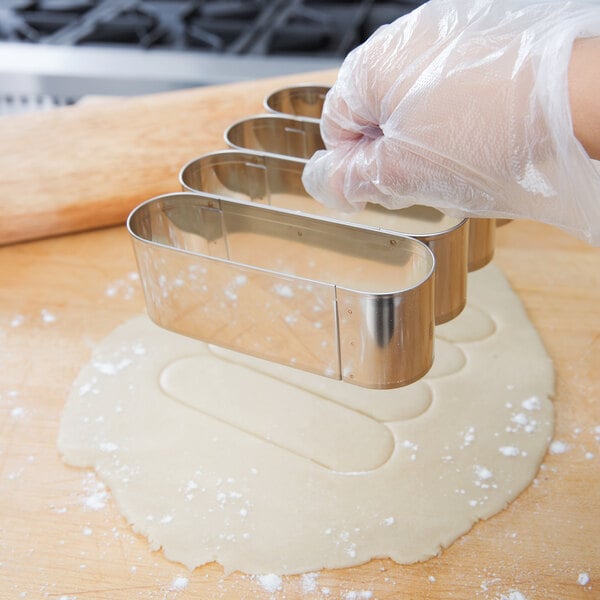 A person in gloves holding an Ateco stainless steel oval dough cutter.