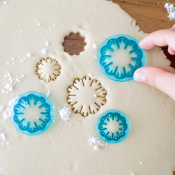 A hand using a blue Ateco carnation cookie cutter to cut dough.