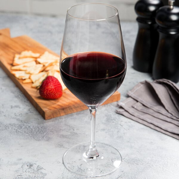 A glass of Chef & Sommelier Bordeaux wine next to a cutting board with cheese and crackers and a strawberry.