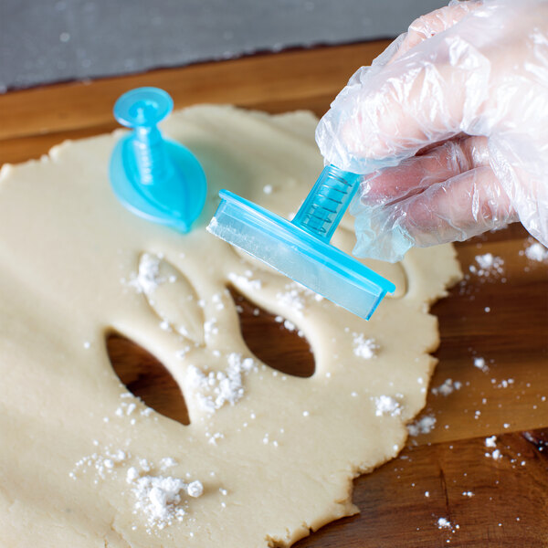 A person using a blue plastic Ateco lily petal cutter to cut dough.
