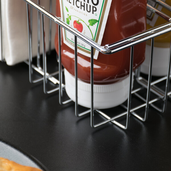 A Clipper Mill chrome metal condiment caddy with a ketchup bottle on a table.