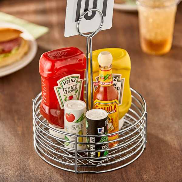 A Clipper Mill stainless steel round condiment caddy on a table with condiments and a ketchup bottle.