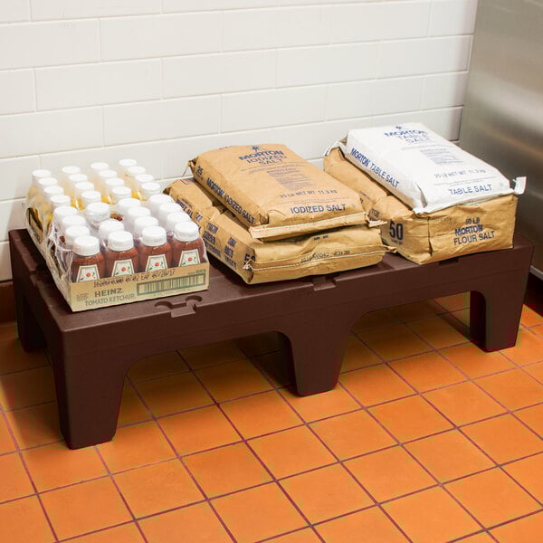 A brown Cambro dunnage rack holding brown bags of food and a bag of salt.