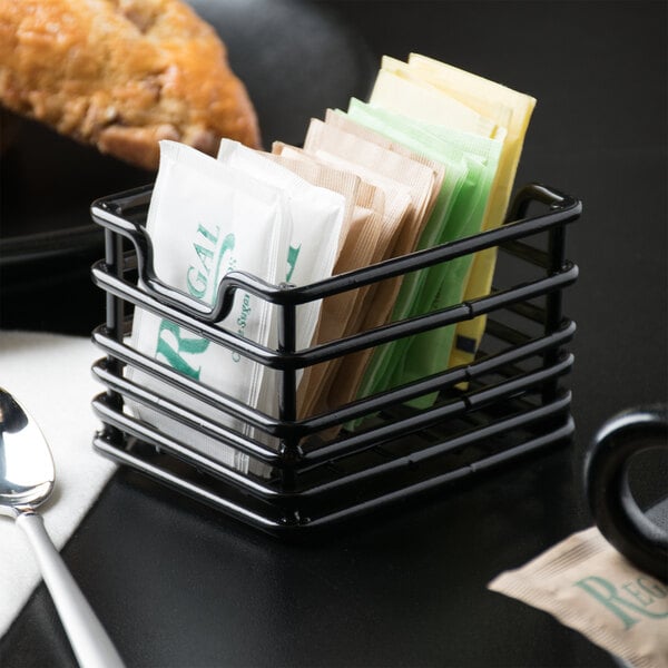 A black Clipper Mill iron sugar caddy on a counter with tea bags inside.