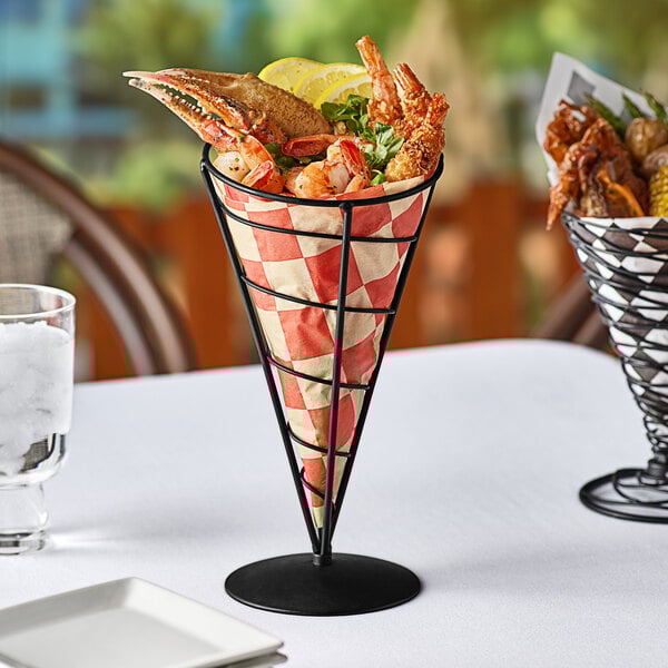 A black metal cone shaped basket with seafood on a table.