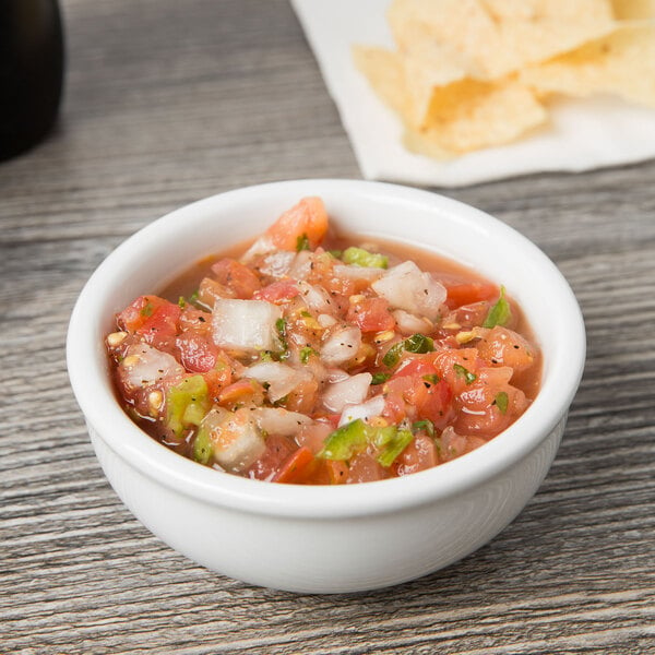 A Tuxton eggshell china bowl filled with salsa and chips on a wood table.