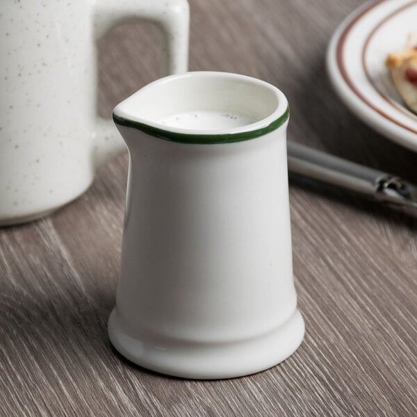 A Tuxton white china creamer with a green rim.