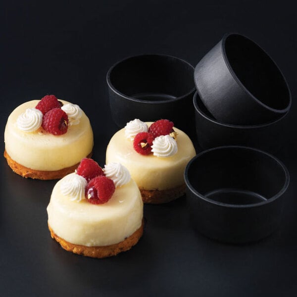 A black Matfer Bourgeat Exoglass mini cake pan filled with small desserts with raspberries and whipped cream.