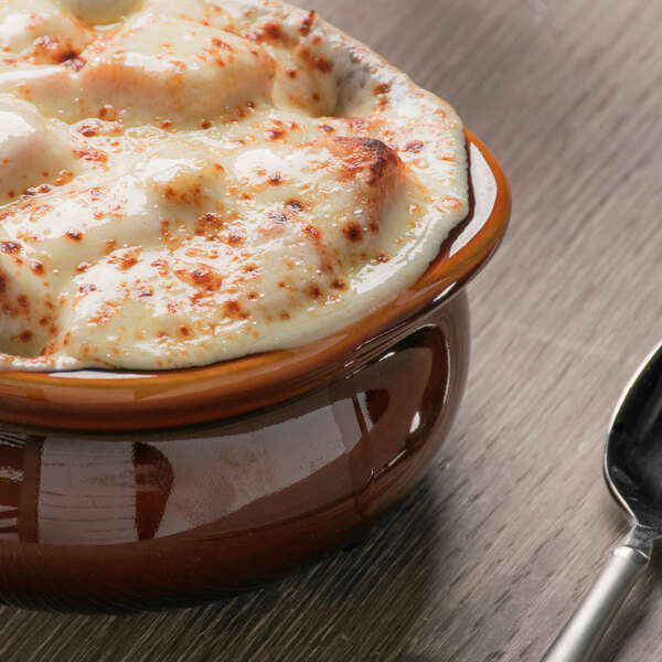 A close up of Tuxton caramel onion soup in a bowl with a spoon.