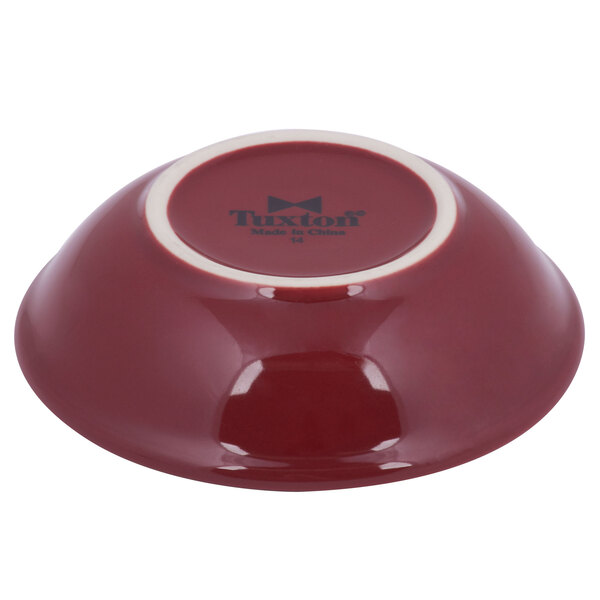 A red Tuxton sauce dish with a white rim.