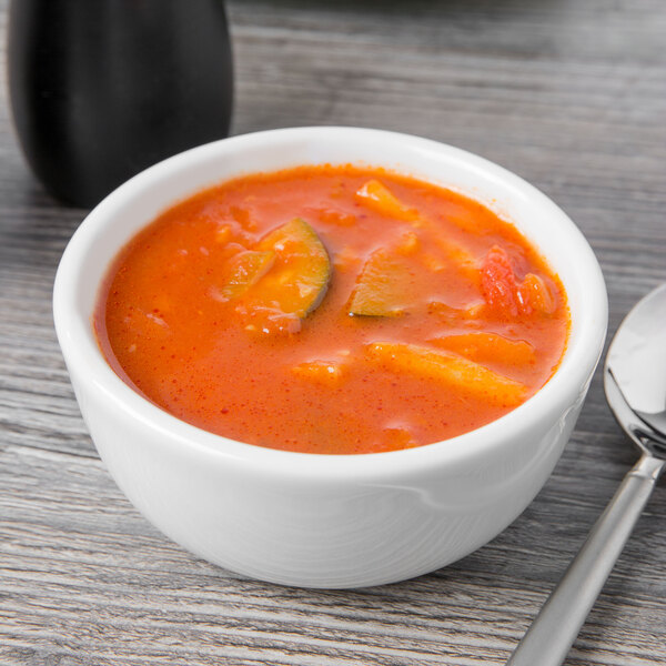 A Tuxton Alaska bright white china bowl filled with soup and a spoon.
