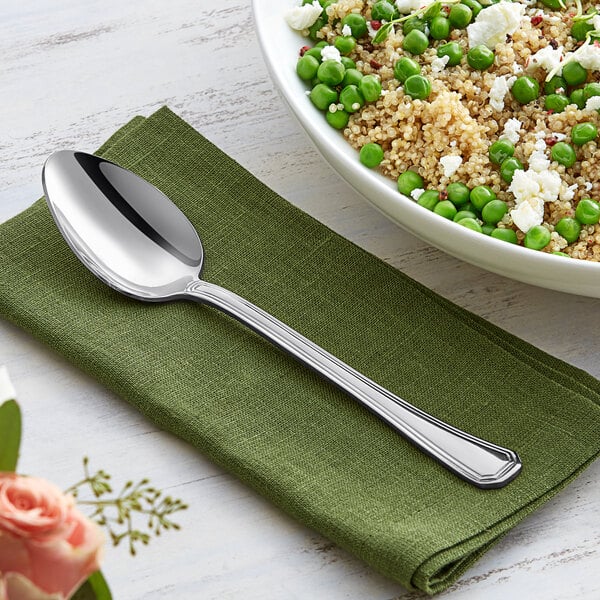 An Acopa stainless steel serving spoon on a napkin next to a bowl of quinoa and peas.