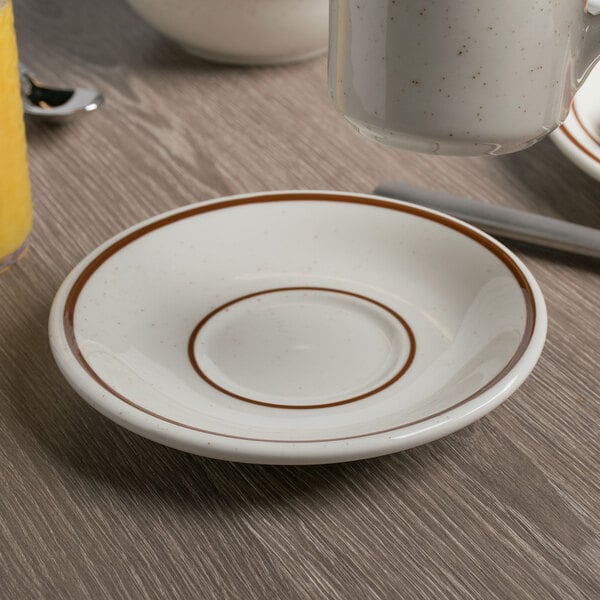 A Tuxton Bahamas brown speckle saucer with a brown rim on a wooden table.