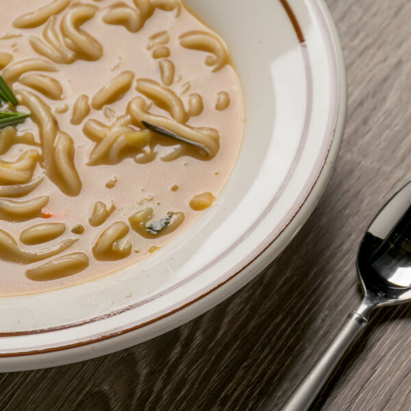 A Tuxton brown speckle soup bowl filled with noodles and herbs on a table with a spoon.