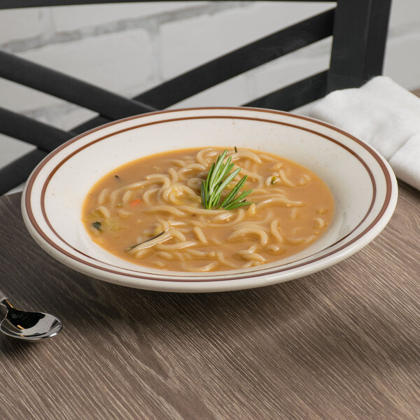 A Tuxton narrow rim brown speckle china soup bowl filled with soup and noodles with a sprig of rosemary on a table.