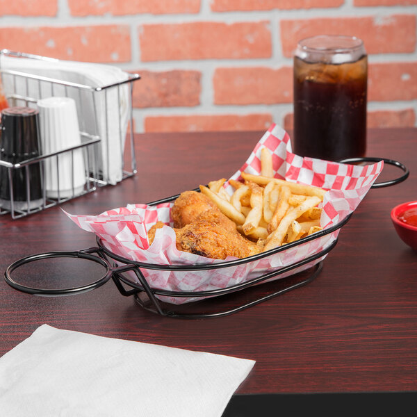 A Clipper Mill black Teflon-coated iron oval basket with fried chicken and french fries on a table.
