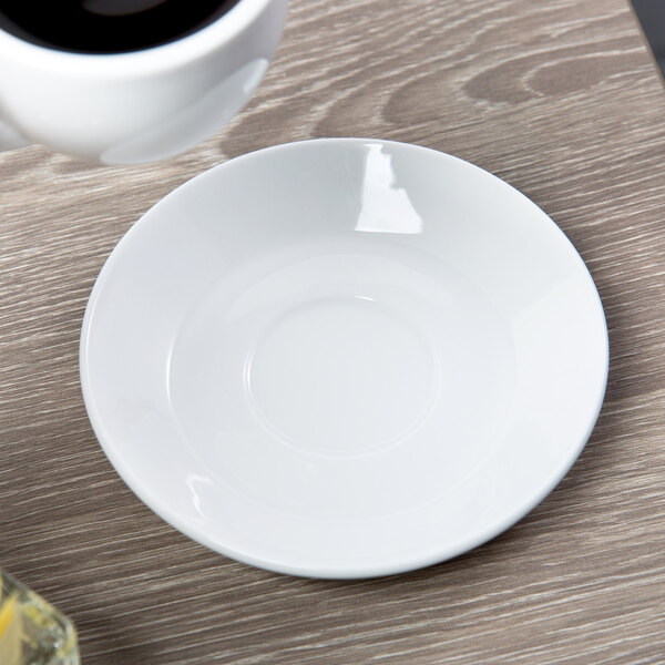 A white Libbey porcelain espresso saucer holding a cup of coffee on a table.