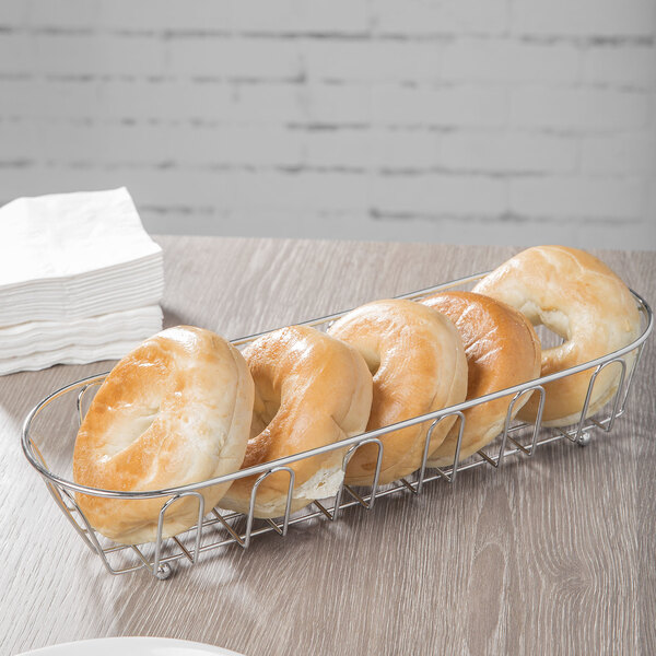 A Clipper Mill chrome metal long oval wire basket holding bagels on a table.