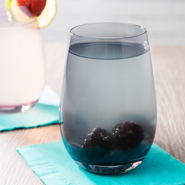 A Stolzle smoky grey stemless wine glass filled with water and blackberries on a white background.