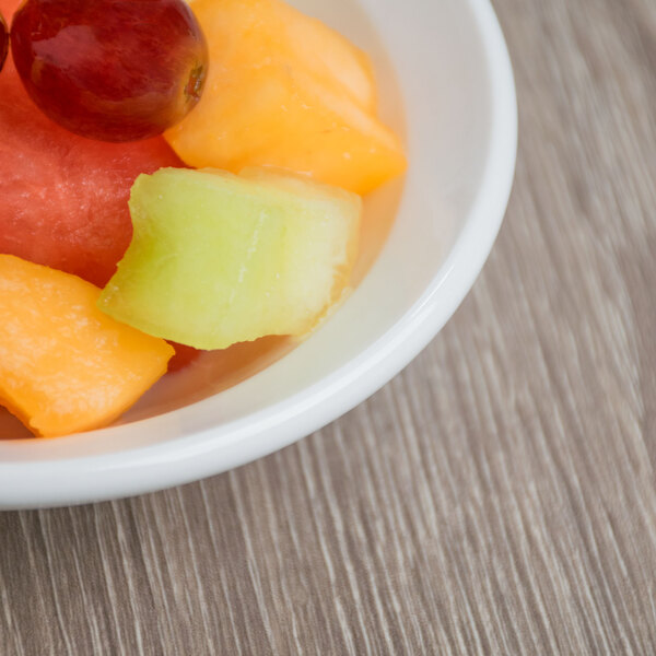 A bright white Libbey porcelain fruit bowl on a table filled with grapes and melon.