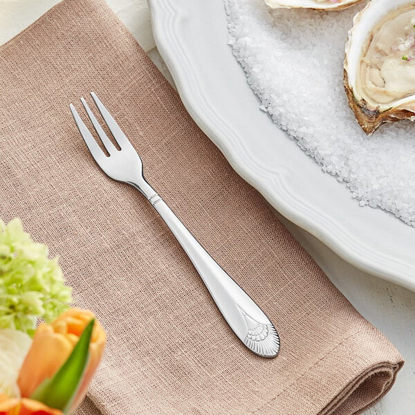 An Acopa stainless steel cocktail fork on a napkin next to a plate of oysters.