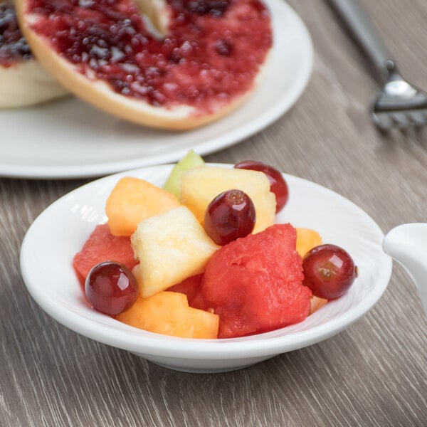 A Libbey bright white porcelain fruit bowl filled with fruit on a table.