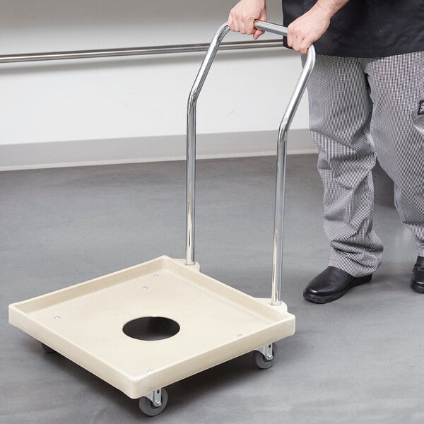 A man using a chrome-plated handle to push a beige Vollrath dish rack dolly.