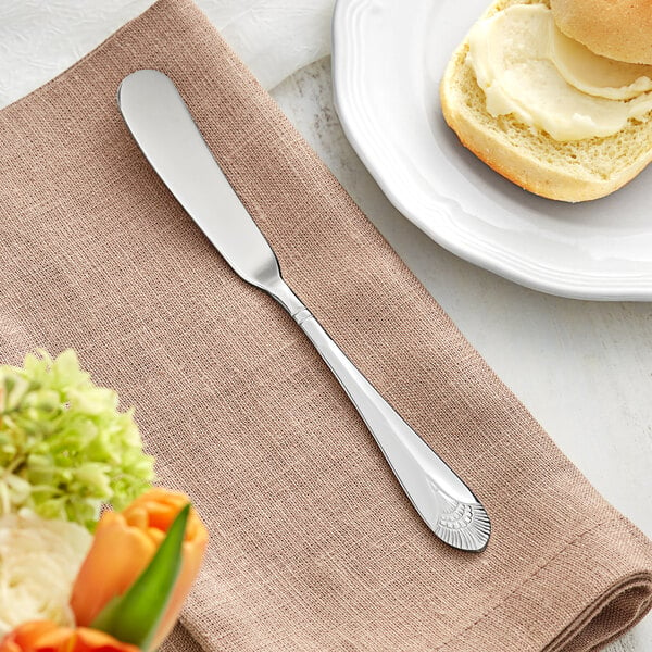 An Acopa stainless steel butter spreader on a napkin next to a plate of bread.