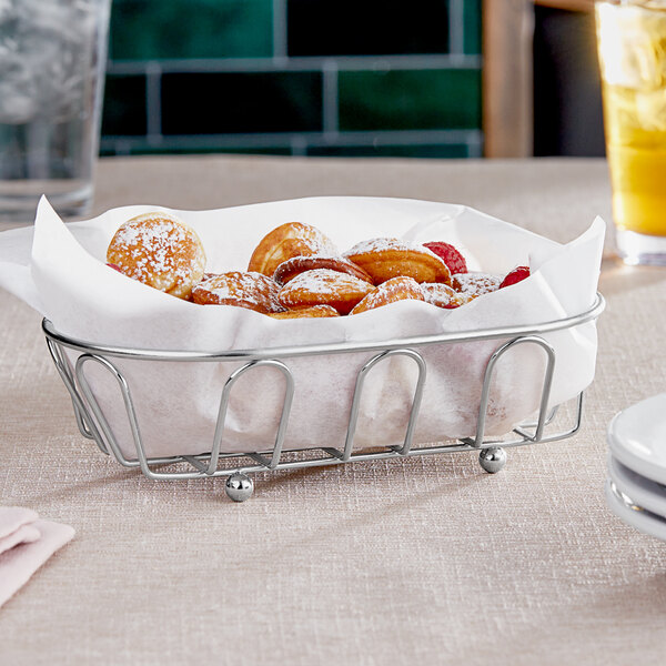 A Clipper Mill chrome metal oval wire basket filled with pastries on a table in a restaurant.