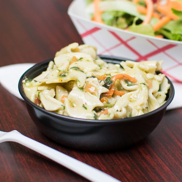 A bowl of pasta and a Solo black wide sauce cup on a plate with salad.