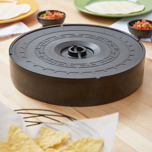 A circular black Carlisle tortilla server on a table with tortillas and salsa.