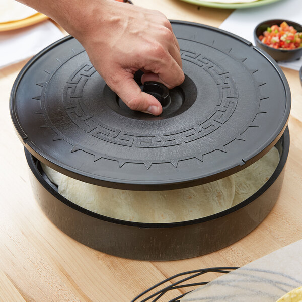 A person's hand holding a black lid to a round black container with food in it.