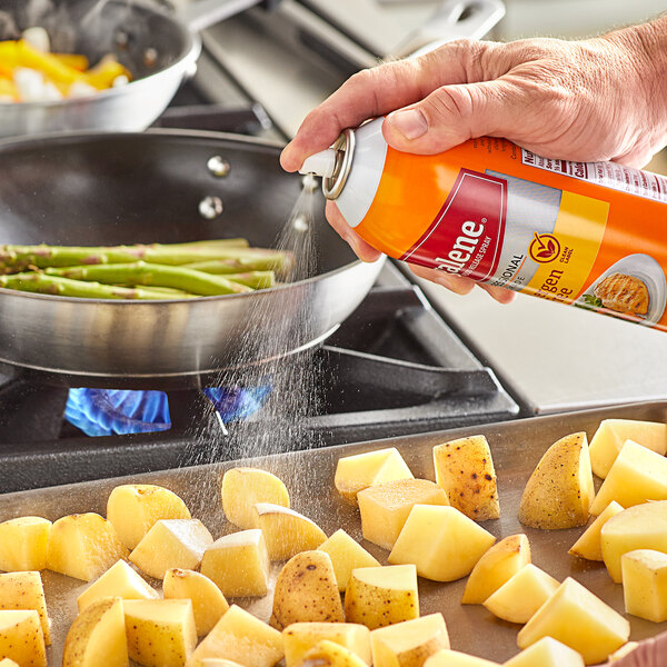 A person spraying Vegalene Canola Release Spray on a pan of potatoes.