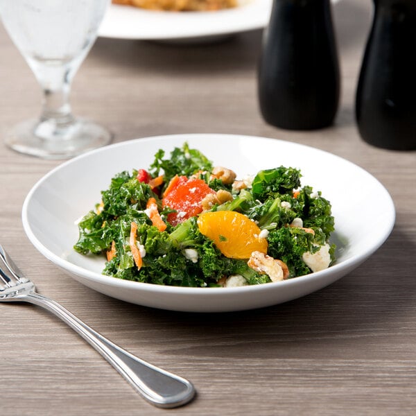 A Libbey white porcelain coupe plate with a bowl of salad with oranges and nuts and a fork.