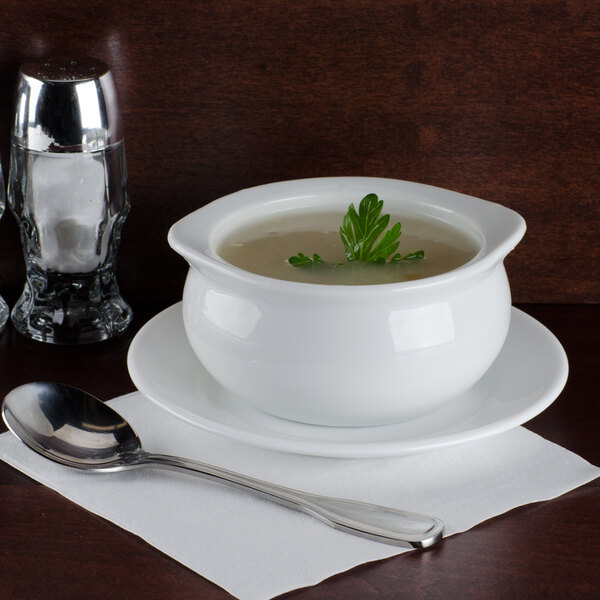 A white bowl of Silver Skillet cream of celery soup with a green leaf in it on a saucer with a spoon.