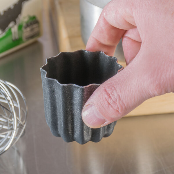 A person holding a small metal Matfer Bourgeat cannele mold.