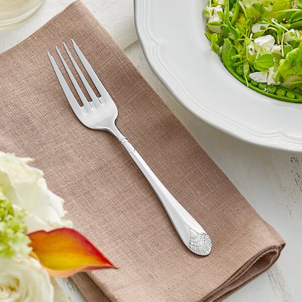 An Acopa Monaca stainless steel salad/dessert fork on a napkin next to a bowl of salad.