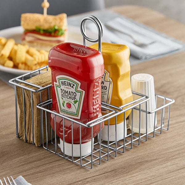 A Clipper Mill chrome metal 4-compartment condiment caddy on a table with ketchup and mustard in it.