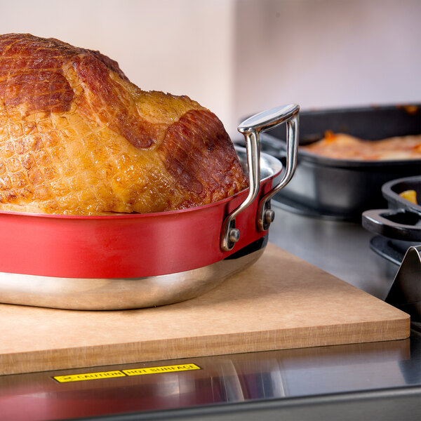 A cooked ham in a pan on a Tablecraft Natural Solid Cutting Board.