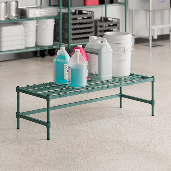 A green metal Regency dunnage rack with containers of liquid on it.