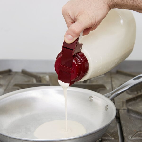 A hand holding a Tablecraft maroon dispenser pouring white liquid into a pan.