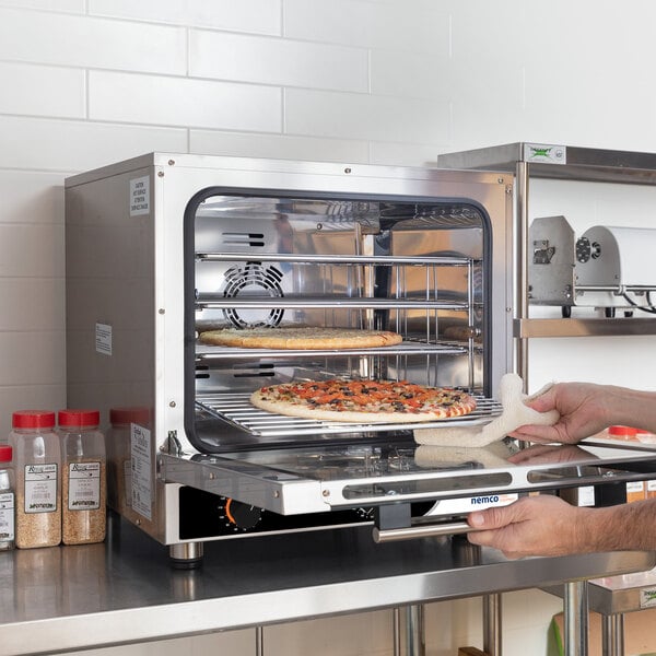 A man using a Nemco countertop convection oven to bake a pizza.