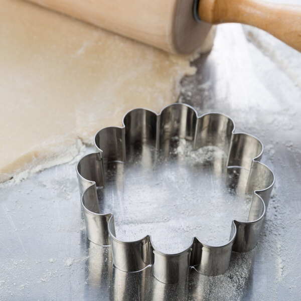 A metal Ateco flower cookie cutter on a table.