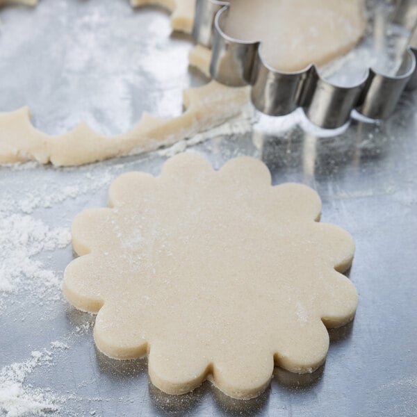 Stainless steel Ateco flower-shaped cookie cutter cutting cookie dough.
