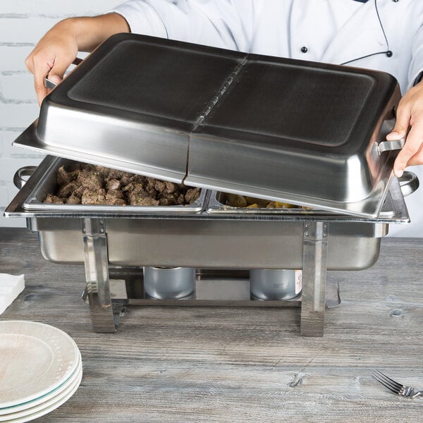 A person using a Vollrath hinged dome cover on a metal serving tray to serve food at an outdoor event.